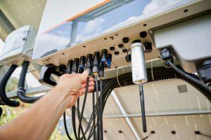 Professional worker connecting wires to solar inverter. Pov of configuring inverter. Male worker turning on PV battery. SSUCv3H4sIAAAAAAAACnRSO2+DMBDeK/U/IM9Bghhc6N6hQ6UO3aoOfhxgxbEj2ySKovz32hhaD+3GfXf+HnfcHh+KAjHqJEfPxS1WoZZKzc5b6qXRAa52K25BC7A5craYVDlAZV6BkN5YSVUOMur5pOkRAqhnpSJ8X5rIeepnBy56WSFOPYyBI4E/FMnwZ6qLrbE0w4vQQq9axBBRfJd13cxi991cwBZUi+JFgx2vaBtJsv9wfkBwbpQJ839wvknHQSmqwczulzB9fP1saATNr0vCLLkFBTQlX0OhoWdDI7AoMWNN2VRDW1KCeSkqxjqBOWm7blFJ1Ohw8WCP+e7oLKTJ1nY2nKo4gDPlk5Vc6jF7Zvy0XHl7xs2svY2W0RYbKWNOlKl4wyFwwoZP1LkwLjY8E+LhHOaY6Wjjl8ArKxLh1LGsMd43fVV1fffUtDWp8TqQfo9JBp7FzkYUan6QIo8uowPUACcE+L6EuhvKph+g7MV+KOsWM4JZ1QtBwgrv3wAAAP//AwDkxVyMBwMAAA==