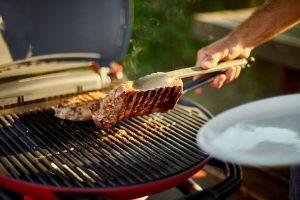 Man put down on a wooden board ready to eat grilled steak meat, male roasted steak meat on the gas grill on barbecue grill outdoor in the backyard, summer family picnic, food on the nature